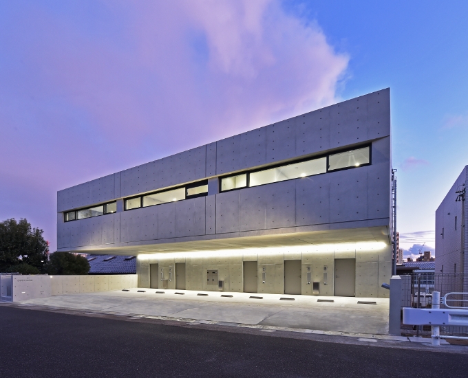 施工事例：横長の窓が連なるコンクリート打ち放しの2階建て建物の夕景